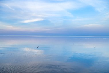 Günbatımında gökyüzü arkaplanı, renkli bulutlar. Deniz suyuna yansıyan doğa soyut kompozisyonu, ufuk çizgisinin doğal mavi mor tonları. Doğa ortamı.