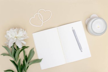 Masanın yukarıdan görünüşü, açık defter, kalem ve aromatik mum ile süslenmiş doğal beyaz şakayık çiçeği. Rahatlama, hayal kurma, plan yapma, sosyal medya için şablon oluşturma zamanı.