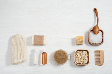 Doğal malzemeden banyo aksesuarları, banyo için sıfır atık seti, jel ve şampuanlı küçük şişeler, sabun, deniz tuzu, beyaz ahşap masadaki bez ve fotokopi alanı.