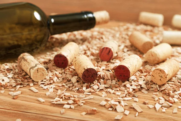 A bottle of wine closed with a stopper on the background of scattered wooden chips and various wine corks. Selective focus.