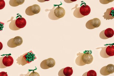 Parlak kırmızı ve altın rengi Noel topları ve soluk pembe arka planda hediye kutusu olan yaratıcı bir Noel çerçevesi. Yeni yıl dekorasyonu, telif alanı olarak yuvarlak oyuncaklar, karanlık gölgeler.