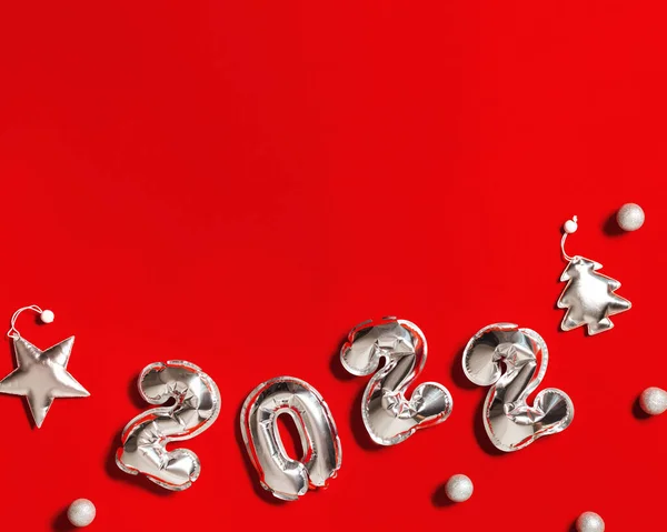 Новий рік 2022 номер срібних кульок і прикраси утворюються як ялинка і срібна зірка на червоному тканинному фоні з місцем для тексту — стокове фото