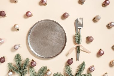 Noel sofrası kurma konsepti, parlak küçük noel topları metal tabakta bej pembe renk, bıçak, çatal desenli yeşil dallar köknar ağacı, yeni yıl bayramı yemeği veya parti fikri, şenlikli dekor