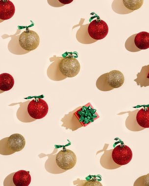 Noel süslemeleri, kırmızı ve altın renkli toplar ve pastel pembe arka planda hediye kutusu. Parlak noel baloları, güneş ışığı, sert gölgeler, minimal stil, düz uzanma