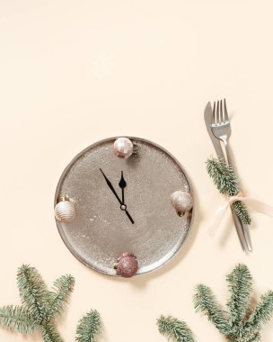 Yeni yıl sofrası, saat elli metal tabaklar ve Noel 'de parlak toplar, bıçak, çatal, bej arka planda yeşil köknar dalları, klasik renkler. Asgari yaratıcı yeni yıl konsepti, gece yarısı