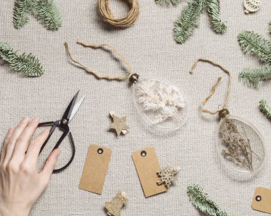 Kurumuş çiçekleri, otları dolduran incik boncuklar. Kırsal kumaş arka planında cam Noel süsleri. Kadınların elinde yeni yıl hediyesi ya da dekorasyon iç mimari fikri, xmas botanik baloları var.