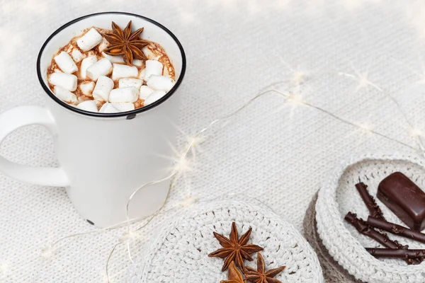 Weiße Tasse heißer Schokolade mit Marshmallows und Süßigkeiten und dekorierter leuchtender Girlande auf gemütlichem Strickhintergrund. — Stockfoto