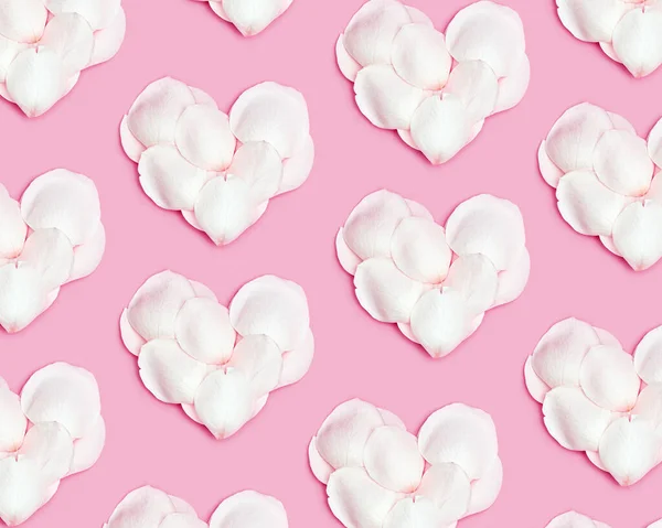 ピンクの背景にバラの花びらで作られた心のパターン。白い花弁からハート形をしています。2月14日の最小バレンタインレイアウト。お祝いのバレンタインデーのコンセプト。平置き、パステルカラー — ストック写真