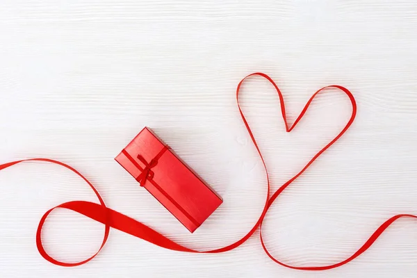Form av hjärta från rött band och röd presentförpackning på vitt trä bakgrund. Glad helgondag. — Stockfoto