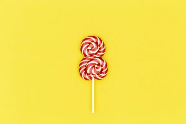 創造的な日の女性の日8の形で甘い赤いロリポップと最小限の組成物。トップビューの休日のお祝い黄色の背景。グリーティングカードデザインソーシャルメディア. — ストック写真