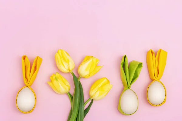 Húsvéti tojás mókás fülekkel nyúl és tavasz sárga friss virágok tulipán rózsaszín asztal másolás hely. — Stock Fotó