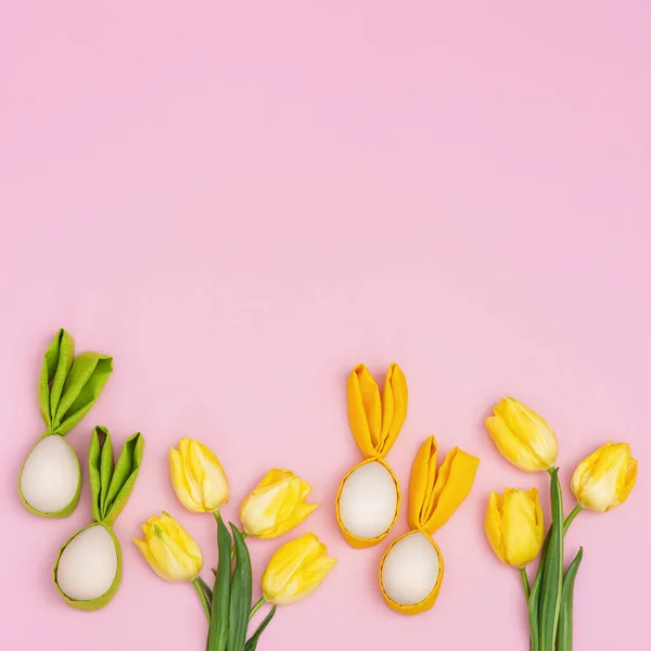 Húsvéti tojás mókás fülekkel nyúl és tavasz sárga friss virágok tulipán rózsaszín asztalon — Stock Fotó