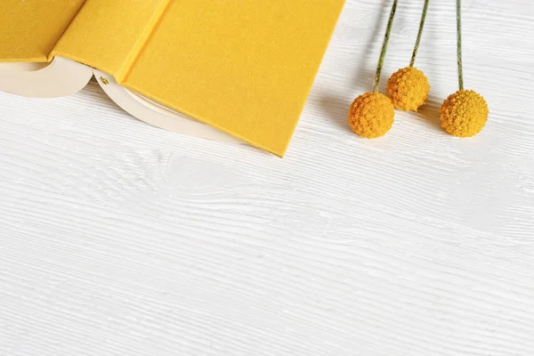 Libro abierto en cubierta amarilla y flores en madera blanca. Concepto de lectura de libros y tiempo sin aparatos —  Fotos de Stock