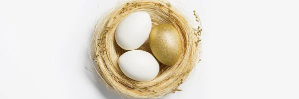 Złoty kolor jaj w gnieździe ze słomy na białym tle. Stylowe złote jajko na wiosenne wakacje. Top widok dekoracyjne błyszczące pisanki Minimalny styl karty — Zdjęcie stockowe