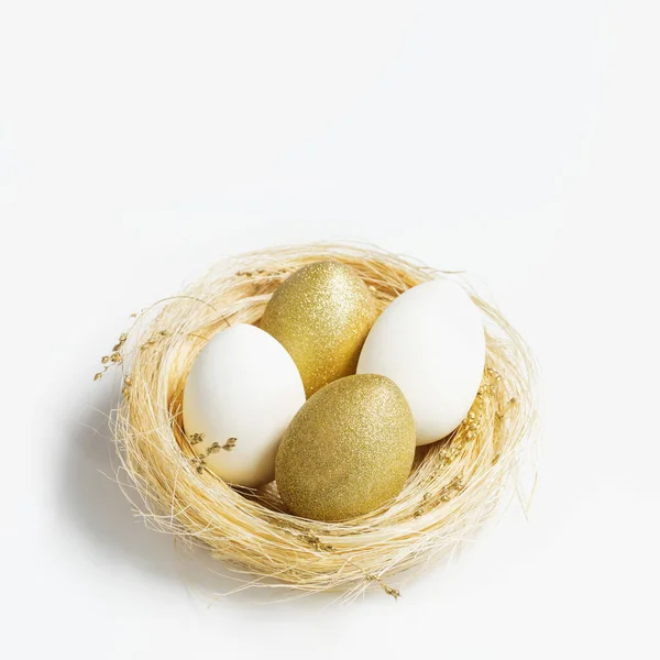 Gouden en witte kleuren eieren in stro nest op witte achtergrond. Stijlvol helder ei voor paasvakantie. Decoratieve glanzende paaseieren minimale stijl kaart met kopieerruimte — Stockfoto