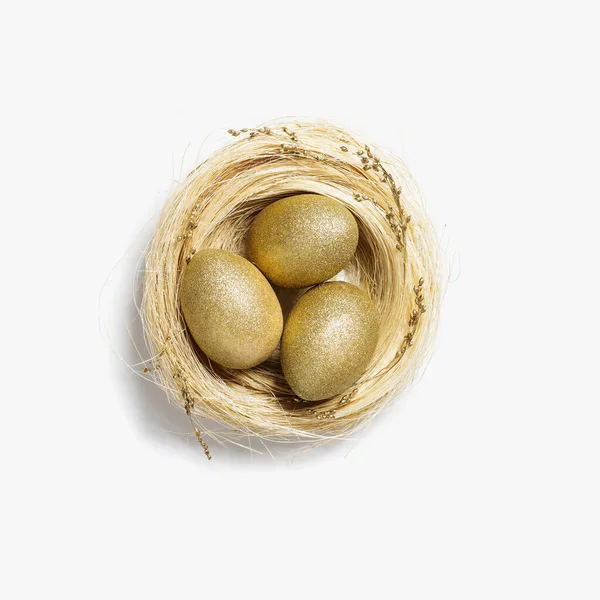 Gouden eieren in nest van stro op witte achtergrond. Stijlvol gouden ei voor pasen voorjaarsvakantie. Top view decoratieve glanzende paaseieren minimale stijl kaart — Stockfoto