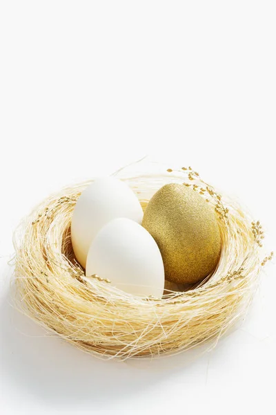 Золотые и белые цвета яйца в соломенном гнезде на белом фоне. Стильное яркое яйцо для весеннего пасхального праздника. Декоративные блестящие пасхальные яйца минимальный стиль карты с копировальным пространством — стоковое фото