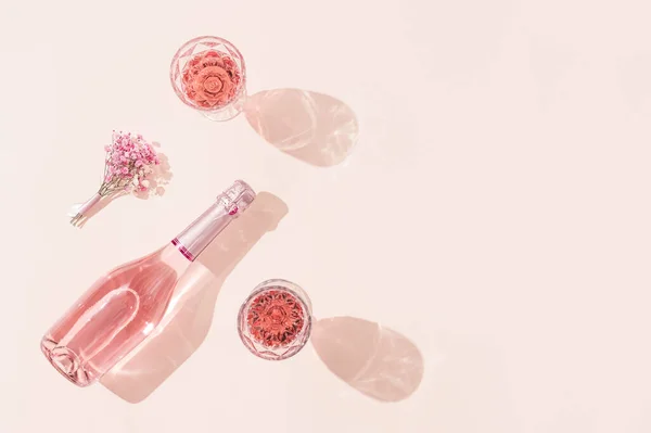 バラのワインのボトル、明るい日差しの中で飲み物、花の小さな花束を持つ2つのメガネ。夏のロマンスの概念. — ストック写真