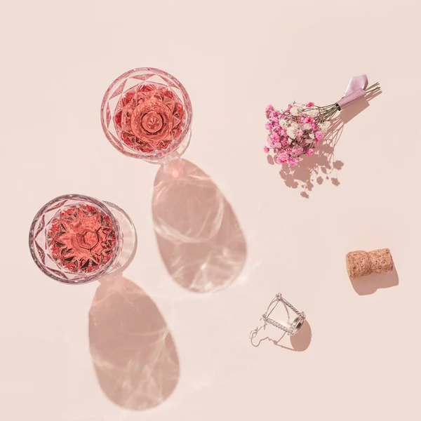 バラのワインとパステルピンクの背景に花の小さな花束の2つのファッショングラス夏休みフラットレイ — ストック写真