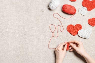Sevgililer günü için kırmızı örülü kalpler, kadın elleri örgü örer. Kalp, kanca, kumaş arka planda iplik, el işi sevgililer günü, romantik bir tatil günü için hediye. Needlecraft evde.