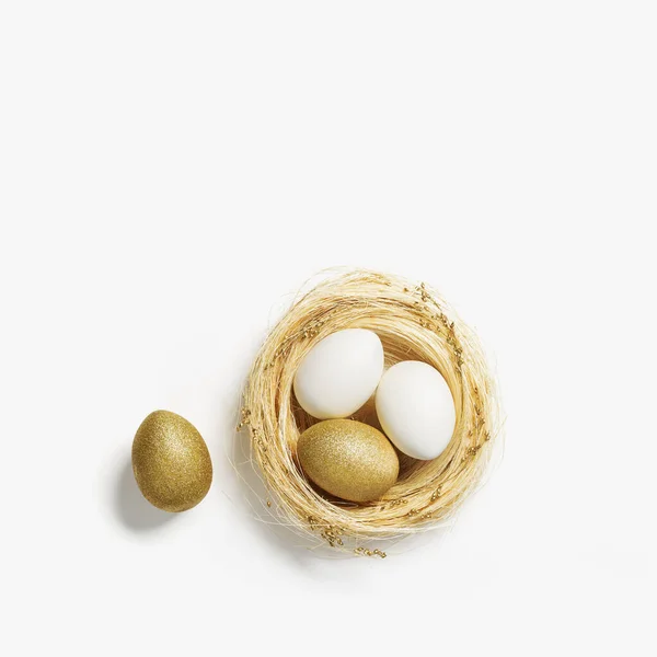 Gouden eieren in nest van stro op witte achtergrond. Stijlvol gouden ei voor pasen voorjaarsvakantie. Top view decoratieve glanzende paaseieren minimale stijl kaart — Stockfoto