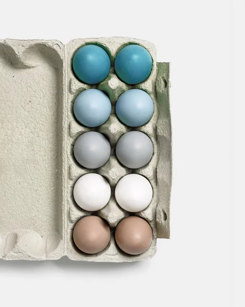 Colorful Easter eggs in carton packing, blue, beige, white neutral colors, festive chicken egg in paper container on lihgt grey colored background. Minimal style aesthetic composition — Stock Photo, Image
