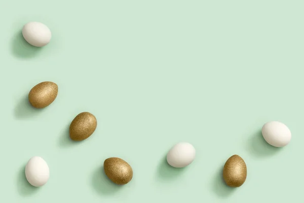 Βαμμένα πασχαλινά αυγά λευκά και χρυσά χρωματισμένα σε ανοιχτό πράσινο χαρτί. Ελάχιστη ιδέα του Πάσχα. Κορυφαία άποψη διακοπές άνοιξη — Φωτογραφία Αρχείου