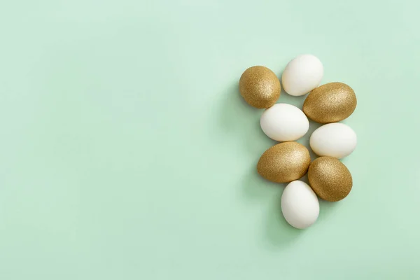 Βαμμένα πασχαλινά αυγά λευκά και χρυσά χρωματισμένα σε ανοιχτό πράσινο χαρτί. Ελάχιστη έννοια του Πάσχα. — Φωτογραφία Αρχείου