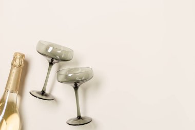 Şampanya bardakları gri camlar, şampanya ya da bej arka planda köpüklü şarap şişesi. Neşeli içki konsepti, parıltı ve güneş ışığı. Modern şarap renkli bardaklar. Yaratıcı düz yatak