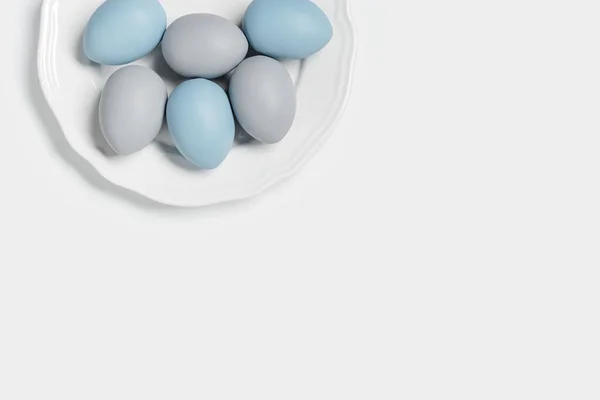 Geschilderde paaseieren blauw, grijs gekleurd op ronde witte plaat, lichte achtergrond met kopieerruimte. Kip ei pasteltinten. Pasen vakantie voedsel, monochroom minimaal design esthetische platte lay — Stockfoto
