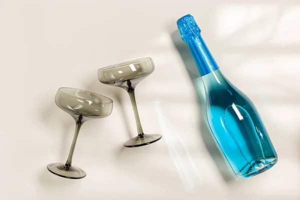 Blaue Champagner- oder Sektflasche, Sektgläser aus getöntem grauen Glas auf beigem Hintergrund. Festlicher Drink Minimalkonzept. Moderne Weingläser, dunkles Glas — Stockfoto
