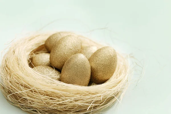Пасхальные яйца светло-золотистого цвета в соломенном гнезде на светло-зеленом. Весенний пасхальный праздник — стоковое фото
