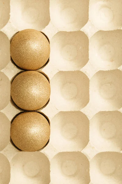 Easter background with bright eggs, shiny golden colored eggs in packaging from carton. — Stock Photo, Image