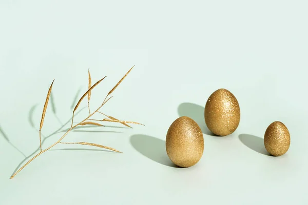 Painted Easter shiny eggs and gold colored plant on light green paper. Minimal easter concept. Spring holiday background — Stock Photo, Image