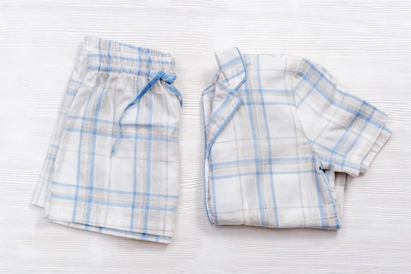 Beyaz ahşap üzerinde mavi çekli ve çizgili katlanmış beyaz pijamalar. — Stok fotoğraf