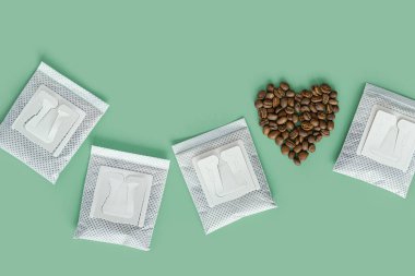 Drip coffee bag and heart from coffee beans, ground coffee for brewing in cup, pack with paper bag drip coffee filter, mint color background, top view, minimal flat lay, pastel color clipart
