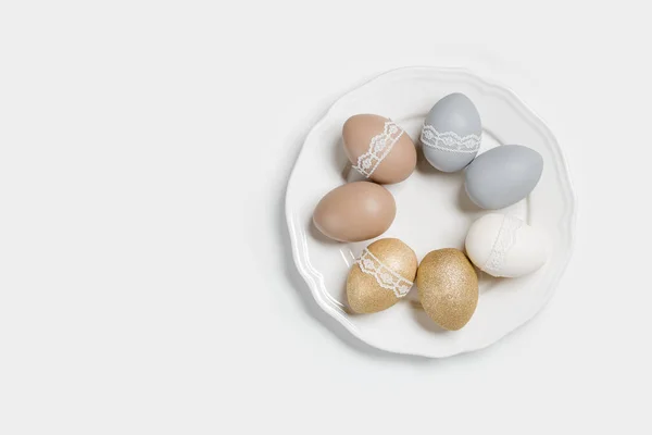 Boyanmış Paskalya yumurtaları, altın sarısı, gri, bej renkli, beyaz plaka, açık arkaplan. Bant dantelli tavuk pastel tonları. Paskalya bayramı yemekleri, minimal tasarım estetik düzlük — Stok fotoğraf