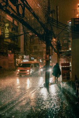 Bangkok, Tayland - Haziran 2022: Yağmurluk giyen bir kişi musonun ortasında Bangkok caddesinde yürüyor. Muson yağmurları.