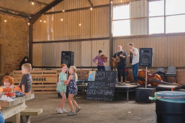 Doğu Neuk, İngiltere - 14 Ağustos 2022: Çocuklar dans ediyor ve yerel halk, Doğu Neuk, Fife, İskoçya 'daki Bowhouse Farmer' s Market 'teki bir ahırda country müzik yapan bir gruptan keyif alıyor.