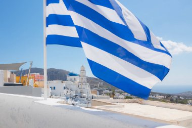 Mavi ve beyaz Yunan bayrağı, Yunanistan 'ın Santorini adasındaki geleneksel Pyrgos Kallistis köyü ve Kurtarıcının Dönüşümü Ortodoks Kutsal Kilisesi üzerinde dalgalanıyor..