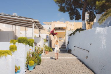 Genç sarışın bir bayan turist Yunanistan 'ın Santorini adasındaki antik Pyrgos Kallistis kasabasındaki geleneksel kaldırım taşı sokaklarını keşfediyor ve geziniyor..