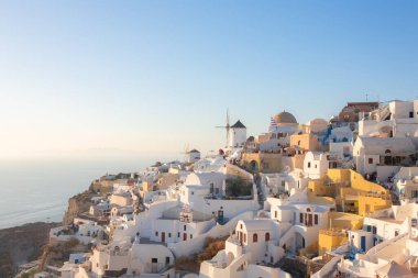 Oia, Yunanistan - 11 Eylül 2022: Yunanistan 'ın Santorini adasında güneşli bir yaz gününde, popüler sahil turizm köyü Oia' da geleneksel beyaz yıkanan binalar ve yel değirmeni manzarası.
