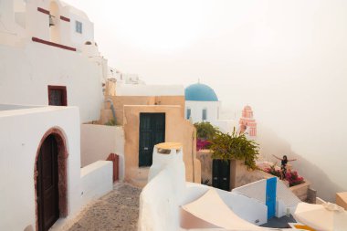 Oia, Yunanistan - 11 Eylül 2022: Yunanistan 'ın Santorini Adası' ndaki Oia köyündeki geleneksel mavi ortodoks kilisesinde, sisli ve puslu bir sabahın ilk saatlerinde bir kadın fotoğraf için poz veriyor..