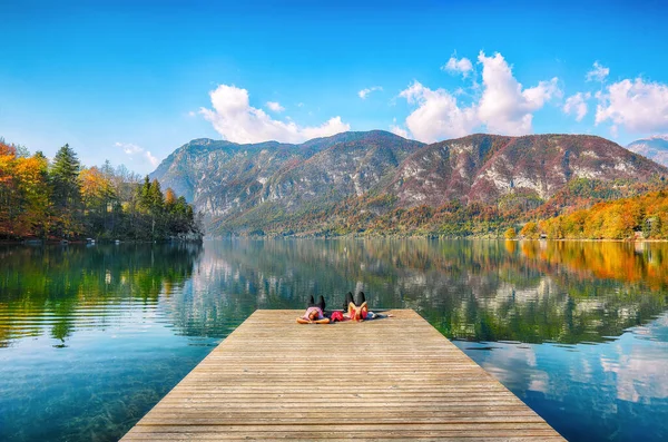 Fabulous view  of  Bohinj Lake with couple lying on a wooden pier . Popular tourist destination Location: Municipality of Bohinj, Upper Carniola region, Triglav National Park, Slovenia, Europe