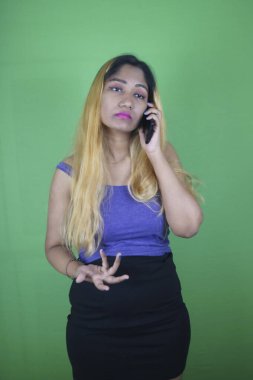 Sarışın kadın yeşil arka planda dururken cep telefonu kullanıyor.