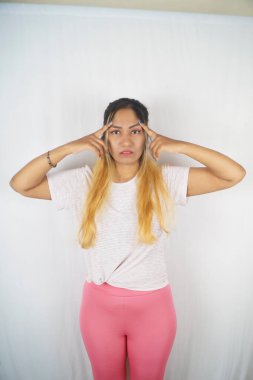 Beyaz arka planda dururken alnına dokunan ciddi bir kadın.