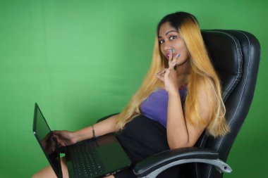 İş kadını yeşil arka planda dizüstü bilgisayar kullanırken el kol hareketi yapıyor