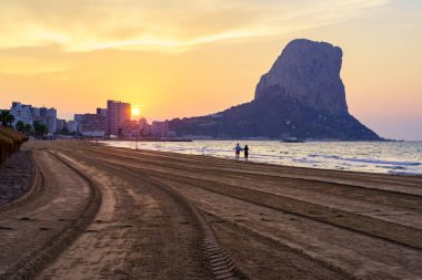 Gün batımında, sahilde yürüyen birkaç kişiyle birlikte beyaz kumsalda. Calpe alicante.