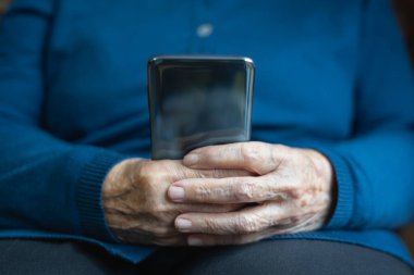 Kıdemli bir kadının elleri cep telefonu tutarken ekrana bakıyor..