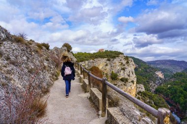Ormandaki yüksek taş duvarların yanında yürüyen bir kadın. Cuenca, İspanya.
